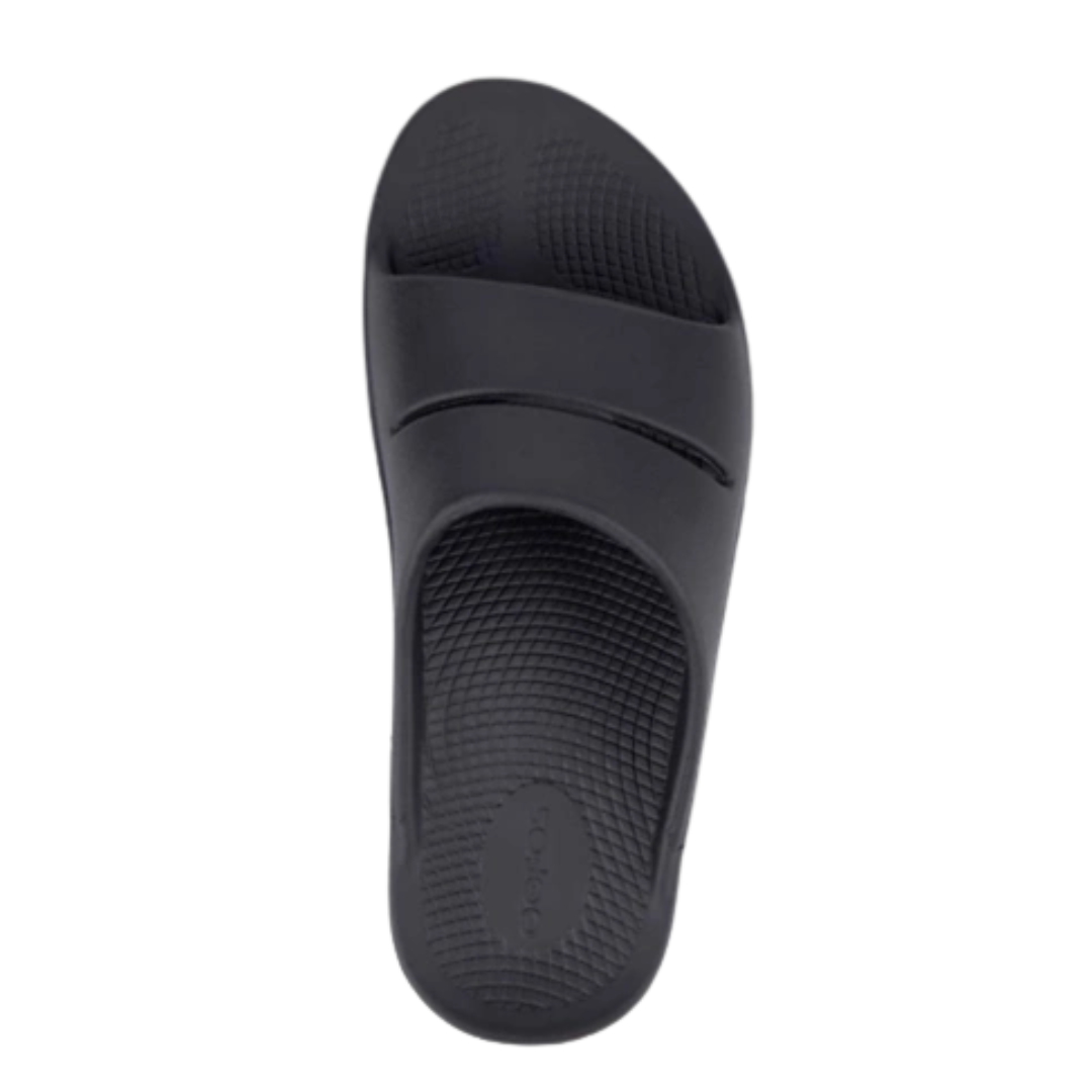 Top view of Unisex OOFOS Ooahh Slide Sandal in black – featuring a wide, seamless synthetic strap, anatomically molded footbed, subtle textured surface for grip, and a clean, minimal look in solid black.